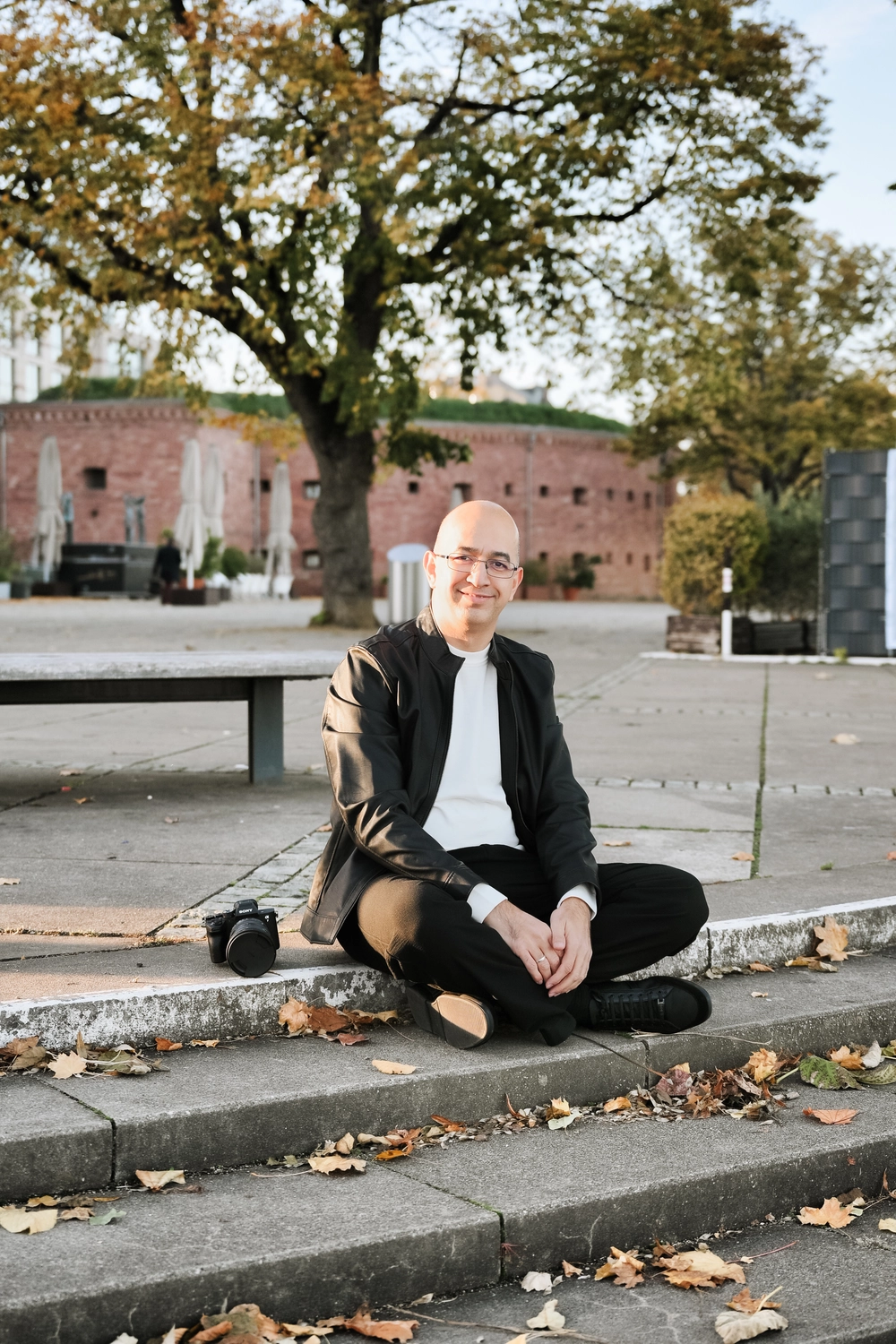 G5 Studios – Fotografie – Bülent Gebes sitzt mit einer Kamera neben sich auf dem Bürgersteig.